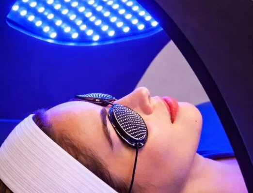Client receiving Glamcor Time Warp LED light therapy facial at Vibrant Med Spa of NWA in Bentonville AR, with blue LED light panel for skin rejuvenation and acne treatment.